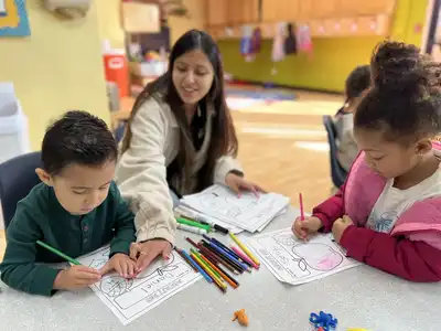 3-year-old children in Kids Adventure Learning Center's Junior Pre-K program doing a hands-on creative learning activity with a smiling teacher